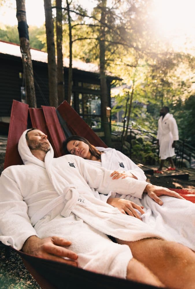 Un couple détendu dans un hamac au cœur de la nature, profitant de l’ambiance apaisante au Scandinave Spa Mont-Tremblant."