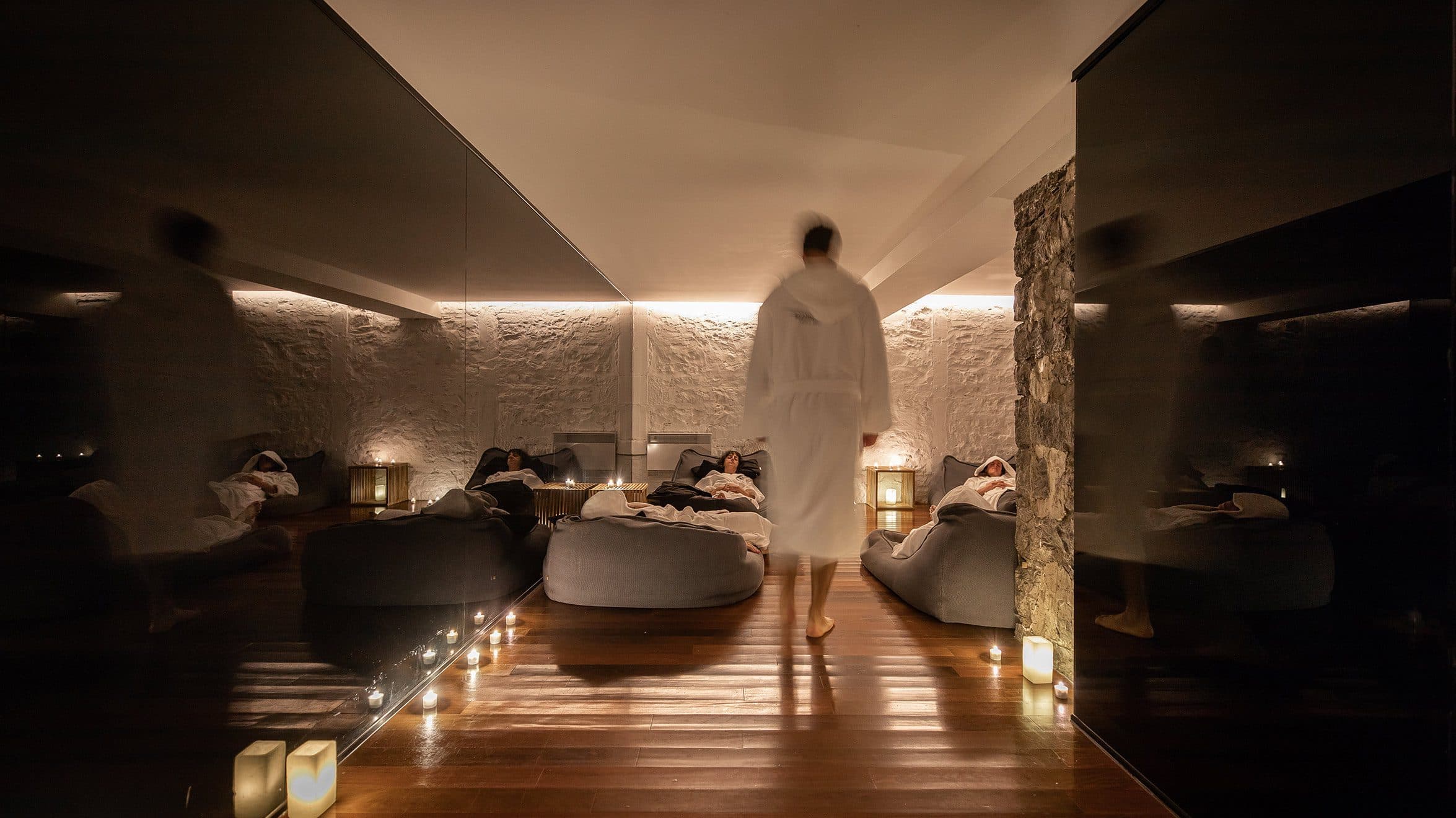 Indoor spa relaxation area with people resting, candles and soft ambient lighting.