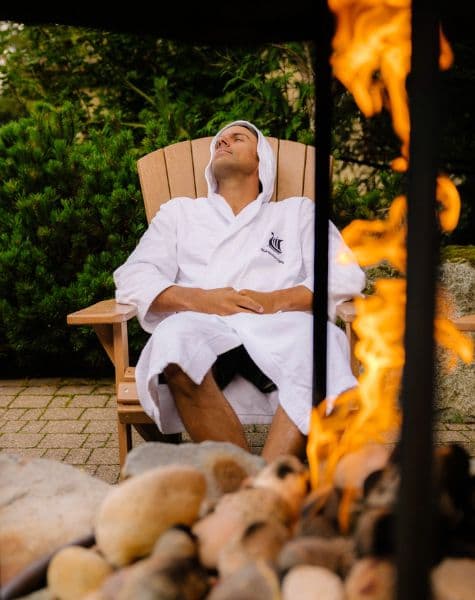 A man relaxing in a chair beside the fire pit, enjoying the warmth and peaceful atmosphere at Scandinave Spa Whistler.