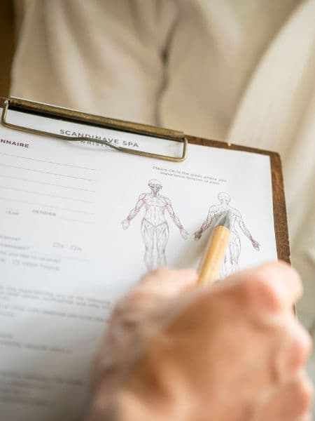hand using pencil to point at back shoulder section of anatomy drawing on a form