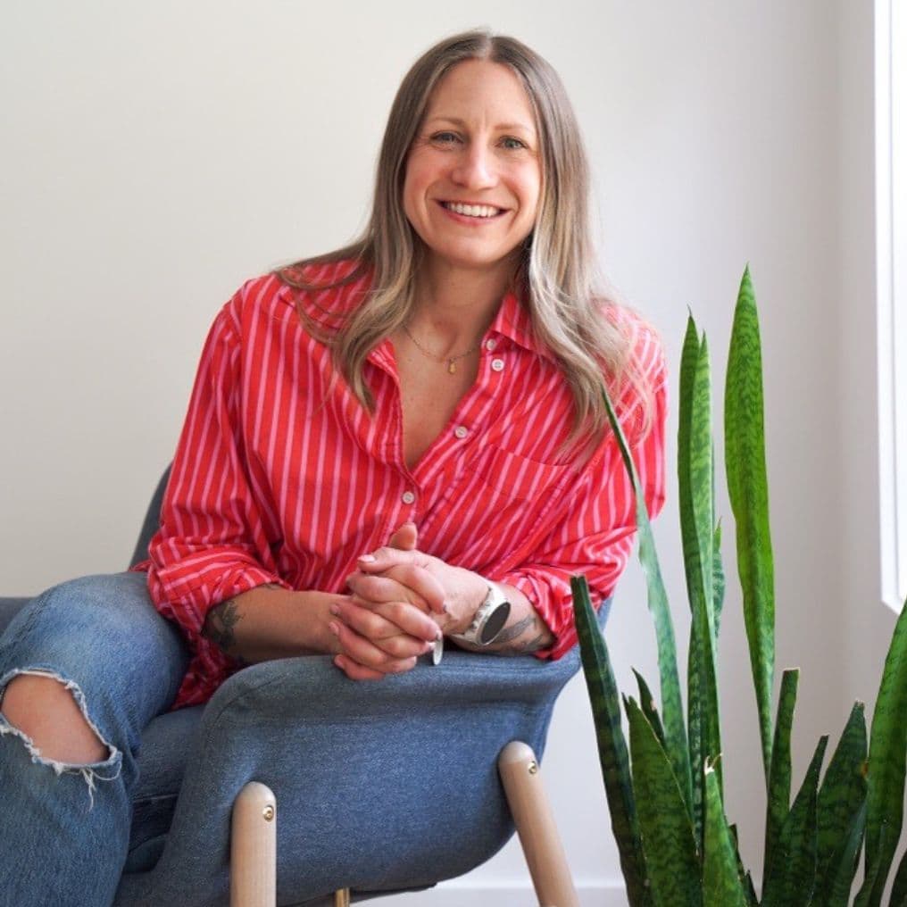 Jessica Robson, Squamish writer and coach, sits in a blue chair wearing a red shirt against a white wall