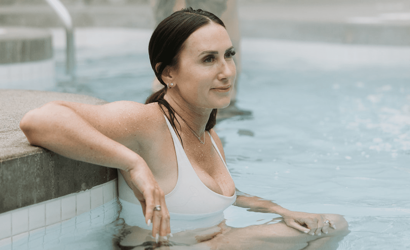 a women lounges in a white bathing suit in the hot pool with her arm up on the ledge at Scandinave Spa Whistler
