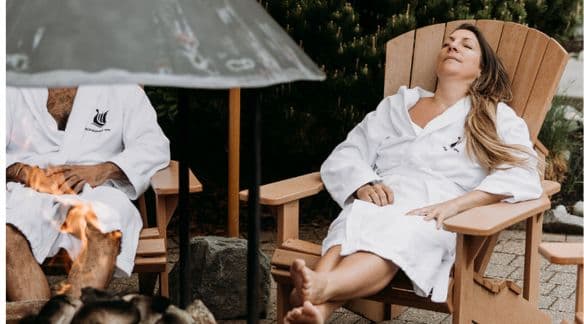 Jane Stoller from Glimmer relaxes on an Adirondack chair in front of the outdoor fireplace at Scandinave Spa Whistler