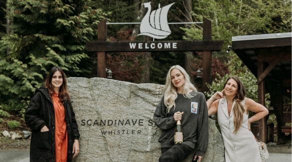 From left to right, standing in front of the entryway outside of Scandinave Spa Whistler is Janet Helou, Marina Billinghurst, and Jane Stoller of Glimmer wine.