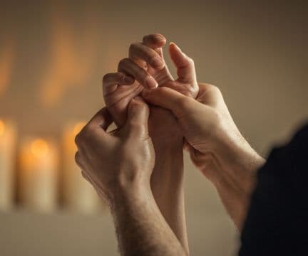 Close-up of a massage therapist massaging a client's hand, with candles in the background.