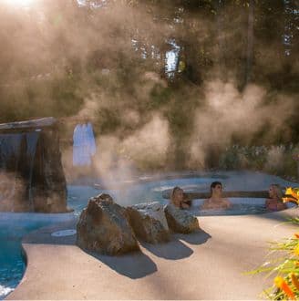 a group of people sit in a hot pool with the sun peeking through the trees at Scandinave Spa Whistler