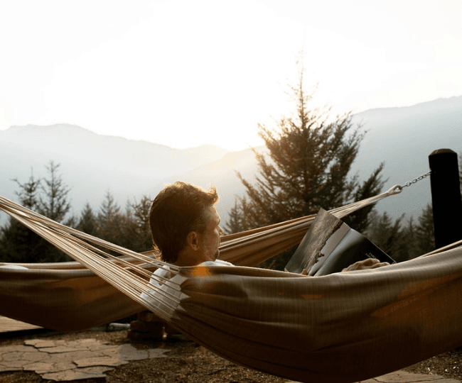 The sun dips down over the mountains while a man lays in a hammock reading a magazine at Scandinave Spa Whistler