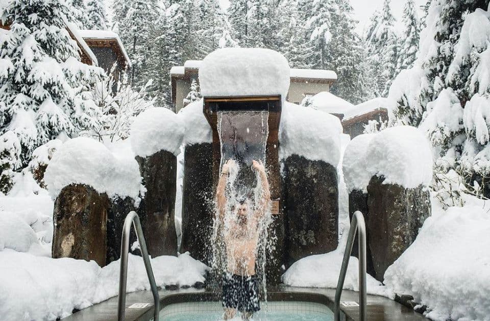 A men under the nordic waterfall at Scandinave Spa Whistler, surrounded by epic snow.
