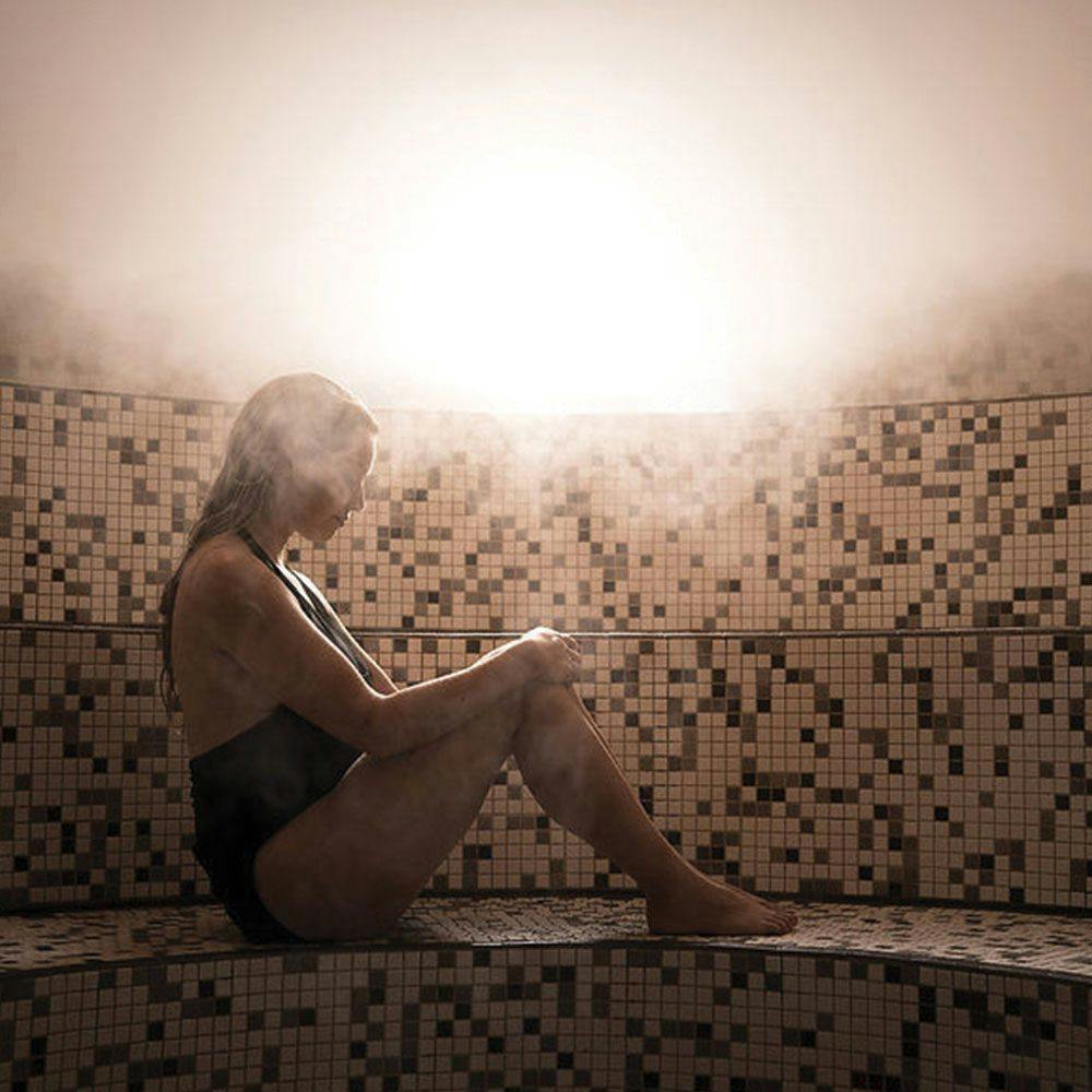 A woman sits in a hot eucalyptus steam room as part of her thermal therapy journey at Scandinave Spa. Heat has many benefits for physical and mental wellbeing as part of the hydrotherapy cycle.