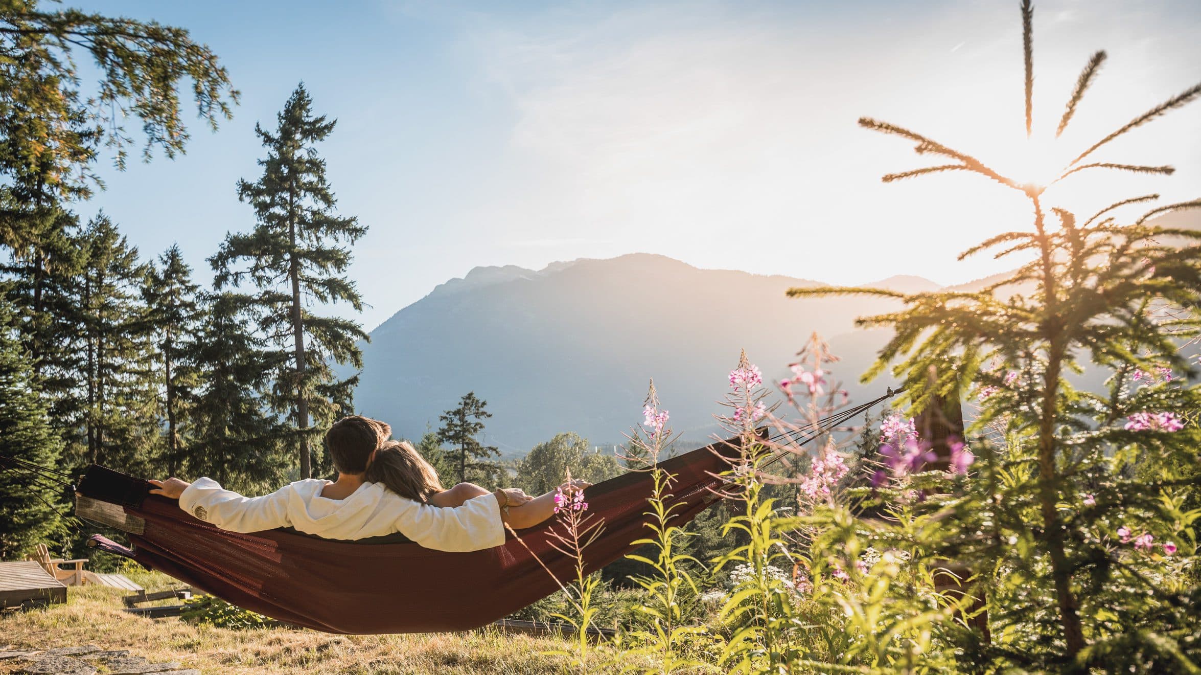 Un couple se détend dans un hamac au Hamac Haven du Scandinave Spa Whistler et profite de la vue majestueuse des montagnes côtières.