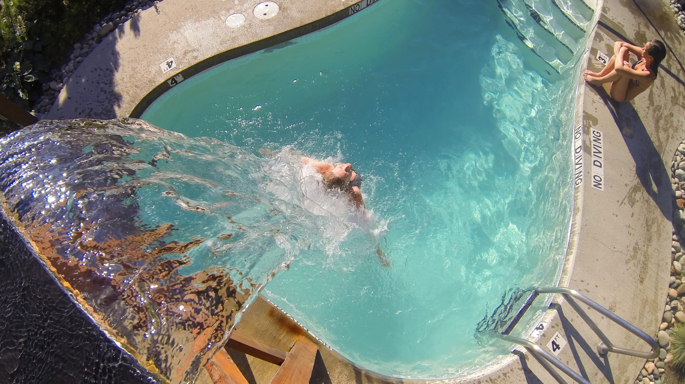 A women under the Nordic waterfall in the summer at Scandinave Spa Whistler.