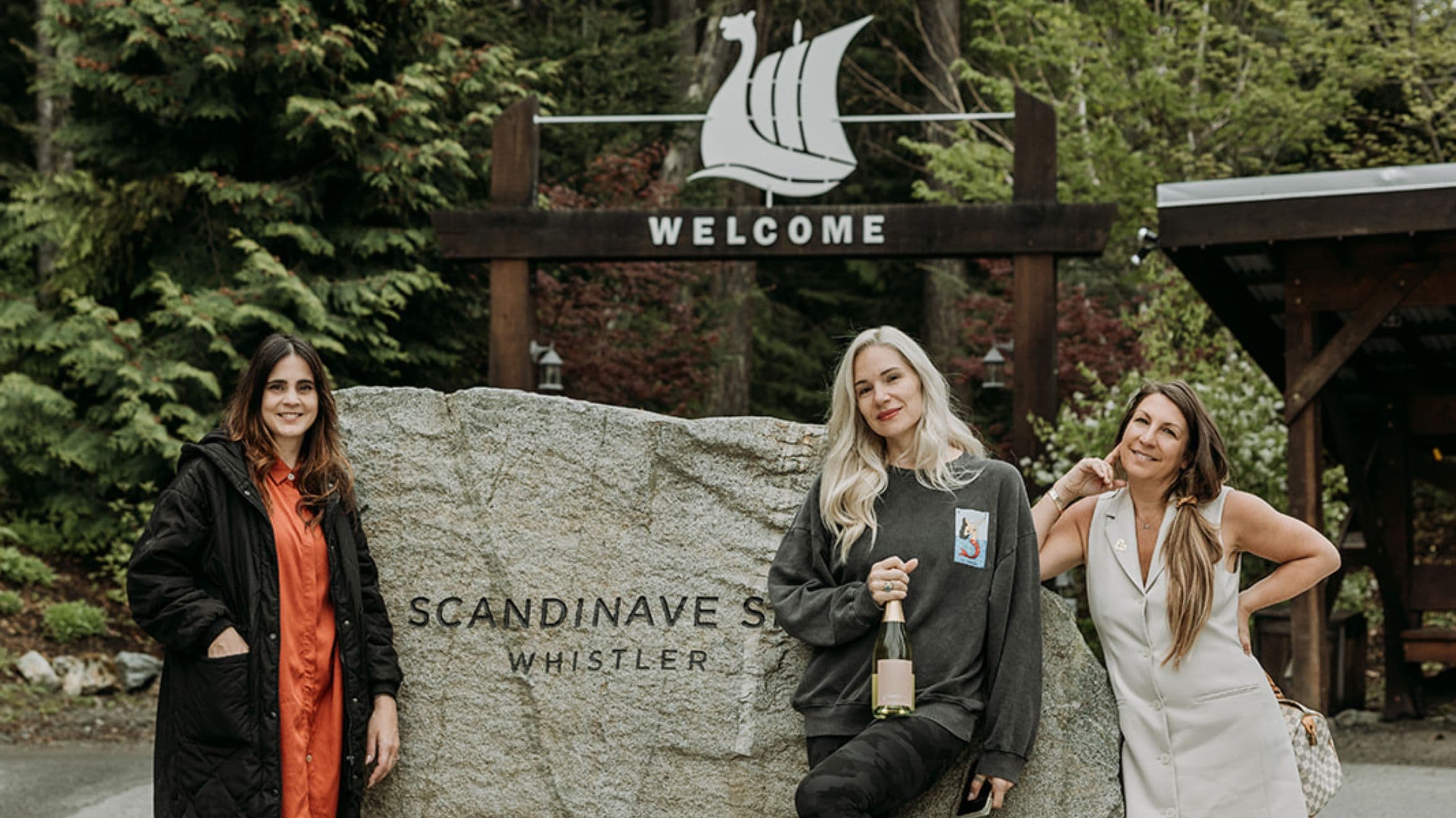 From left to right, standing in front of the entryway outside of Scandinave Spa Whistler is Janet Helou, Marina Billinghurst, and Jane Stoller of Glimmer wine.