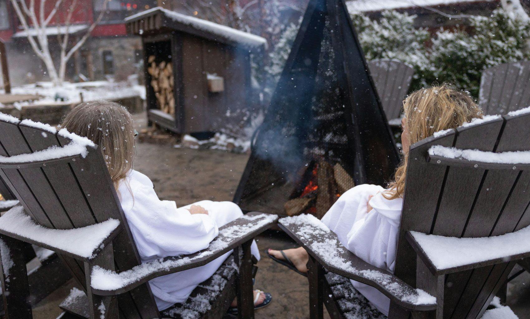 women relaxing around the outdoor fireplace at Scandinave Spa Blue Mountain.