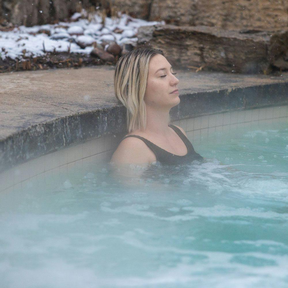woman relaxing in an outdoor hot Bath in winter at Scandinave Spa Blue Mountain.