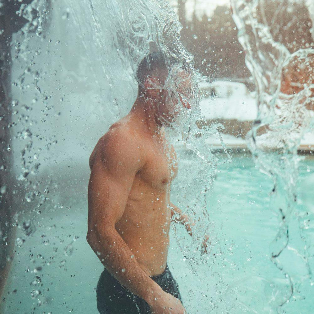 man under cold waterfall at Scandinave Spa Blue Mountain.