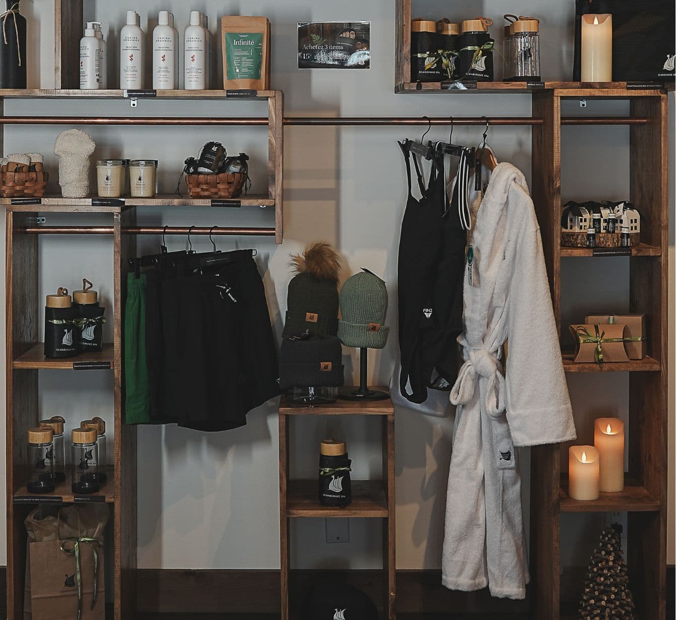 Shelves with boutique items at Scandinave Spa, including Carina Organics products, candles, men’s and women’s swimwear, tea sachets, and a white bathrobe.