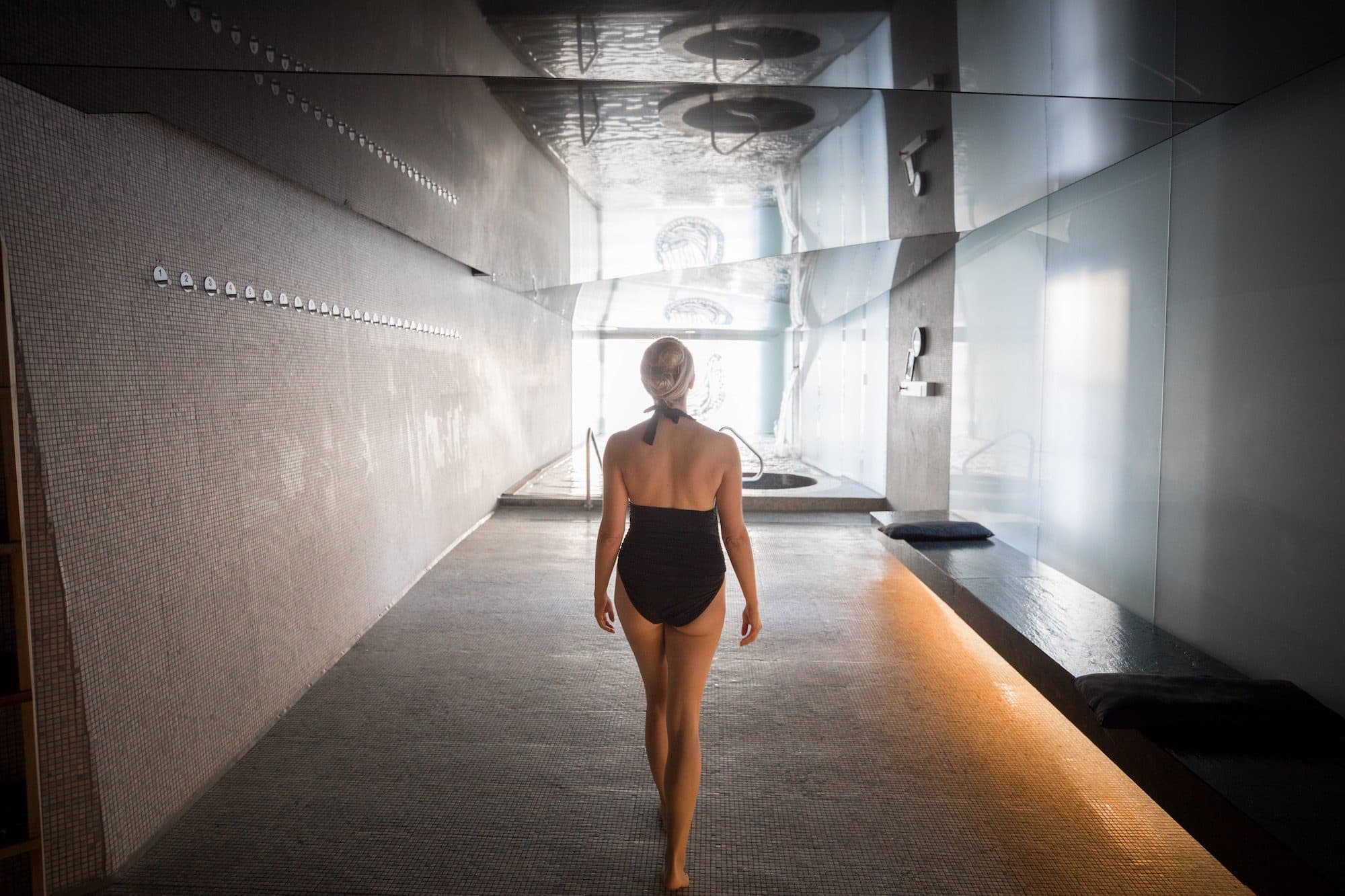 Woman in a black one-piece bathing suit walking through Scandinave Spa Old Montreal, a stylish indoor spa offering hydrotherapy and massage.