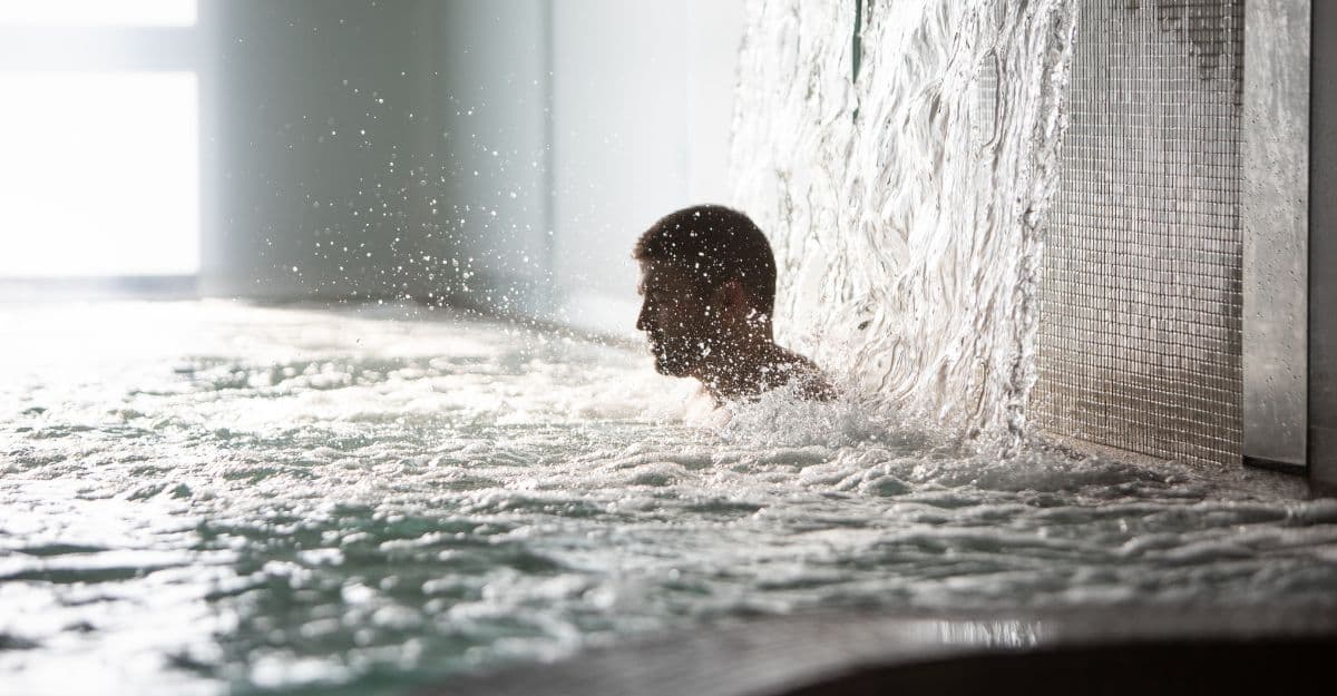 A man in the hot pool under a waterfall, with soft light at Scandinave Spa Vieux-Montréal.