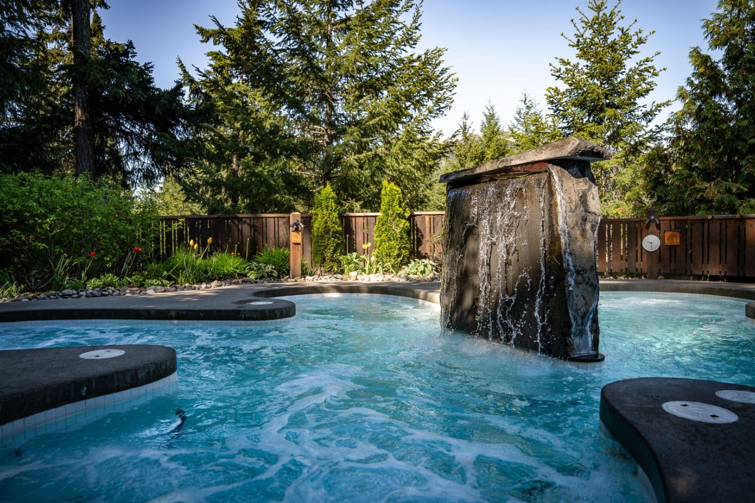 Hot pool with cascading waterfall nestled in nature at Scandinave Spa Whistler, part of the thermal therapy experience.