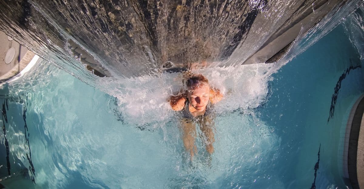 A woman relaxing in the hot pool, enjoying the soothing waterfall at Scandinave Spa Whistler.