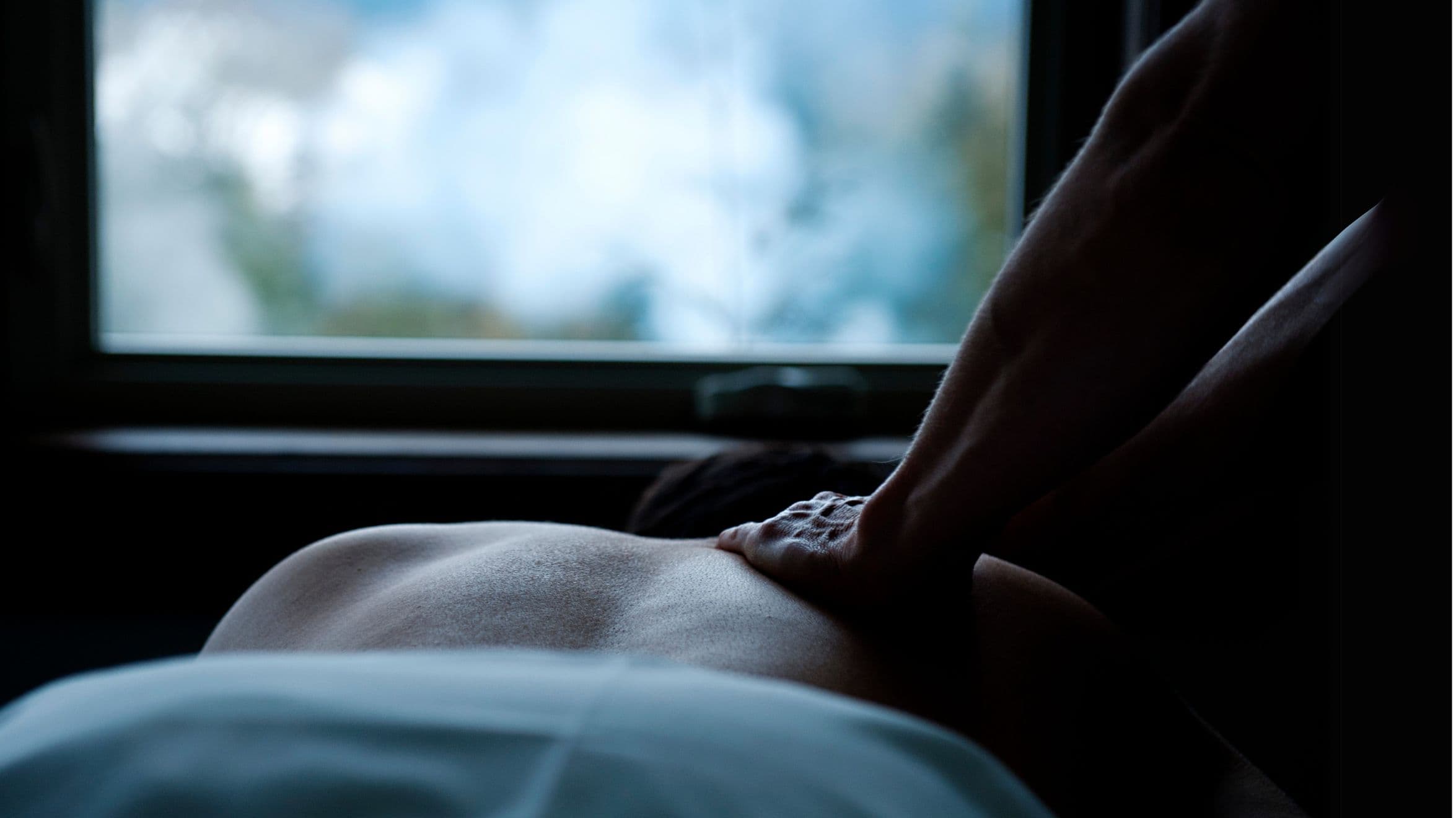 A pair of hands gently massaging the back of a guest at Scandinave Spa Whistler, with a peaceful view through the window.