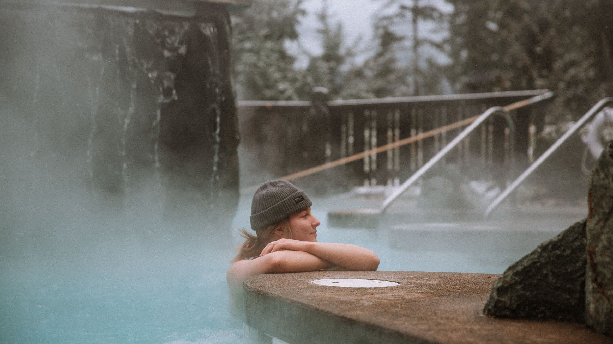 A woman relaxing in the hot pool at Scandinave Spa Whistler during winter, surrounded by snow and peaceful nature.
